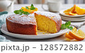 A delicious homemade orange cake, lightly dusted with powdered sugar and garnished with fresh mint and orange slices, with a slice removed, showcasing its moist texture on a white plate 128572882