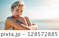 A captivating portrait of a woman with bright blue eyes, her skin glowing and slightly dewy, sitting on a beach with a soft, sun-drenched background, conveying natural beauty and tranquility 128572885