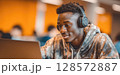 A young man wearing headphones is intently focused on his laptop, suggesting deep concentration while studying, working, or enjoying multimedia content in a modern setting. 128572887