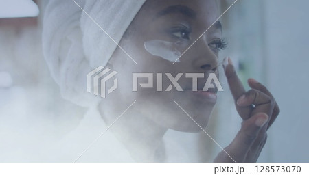 Image of african american woman using cream on face over light spots 128573070