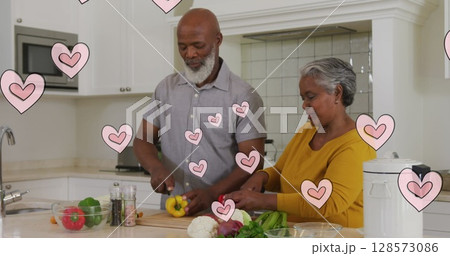 Image of pink hearts over happy african american senior couple preparing food in kitchen 128573086
