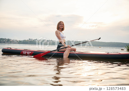 Against cloudy sky. Young woman is on sup boards in the lake 128573483