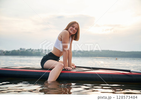 Against cloudy sky. Young woman is on sup boards in the lake 128573484