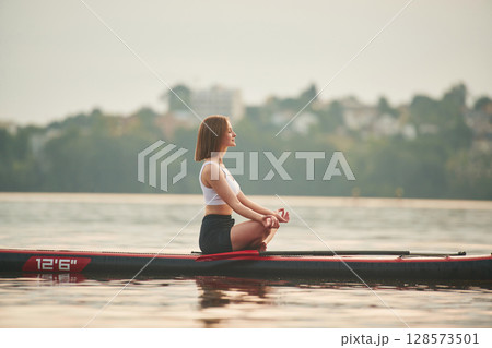 Sitting in lotus pose. Young woman is on sup boards in the lake 128573501
