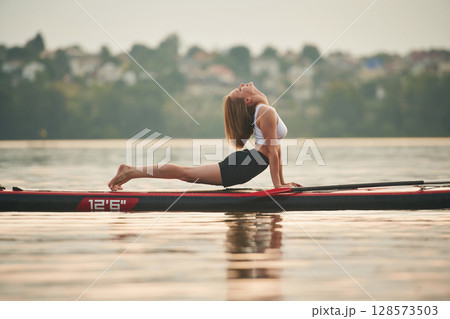 Doing fitness exercises. Young woman is on sup boards in the lake 128573503