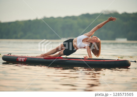 Doing fitness exercises. Young woman is on sup boards in the lake 128573505