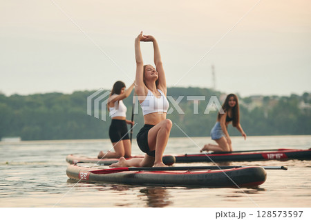 Warm up exercises. Young women are on sup boards in the lake 128573597