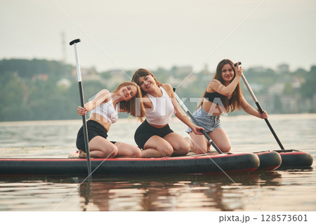 Friends are sitting and having fun. Young women are on sup boards in the lake 128573601