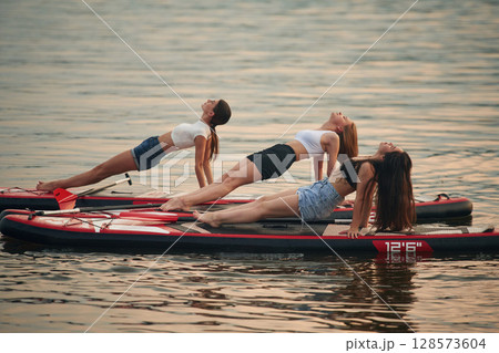 Yoga exercises. Young women are on sup boards in the lake Yoga exercises. Young women are on sup boards in the lake 128573604