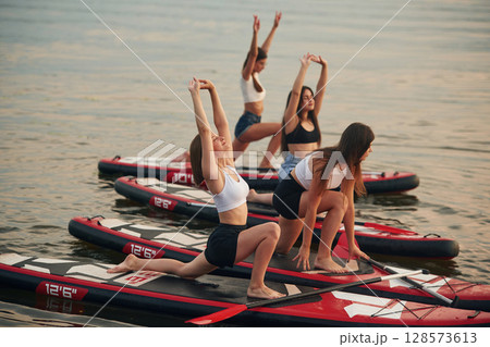 Yoga exercises. Young women are on sup boards in the lake 128573613