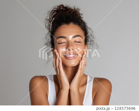 Smiling young woman with luminous skin, exuding a sense of peace and well-being. Her eyes are closed in bliss, showcasing healthy, moisturized skin and natural beauty. Themes of skincare, wellness 128573696