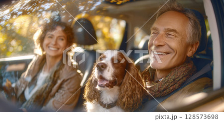 Heartwarming scene of elderly couple with their happy dog, springer spaniel, sharing a moment of pure joy during scenic car journey, bathed in warm autumn. Themes of travel, companionship, happiness 128573698