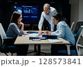 Senior executive mentoring junior colleague in modern office with presentation screen 128573841