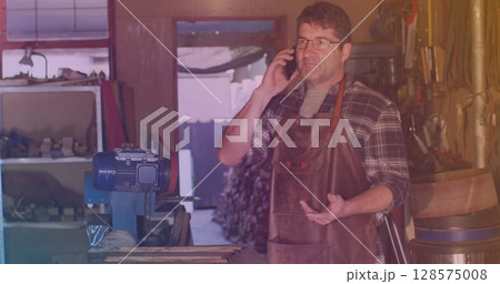 Image of caucasian male worker talking on smartphone in workshop Image of caucasian male worker talking on smartphone in workshop 128575008