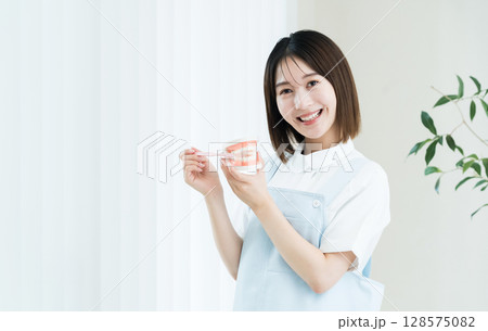 歯ブラシと歯の模型を持つ歯科スタッフの女性 128575082