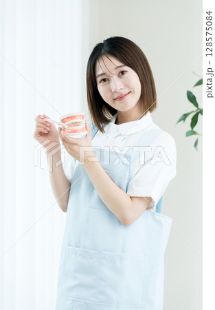 歯ブラシと歯の模型を持つ歯科スタッフの女性 歯ブラシと歯の模型を持つ歯科スタッフの女性 128575084