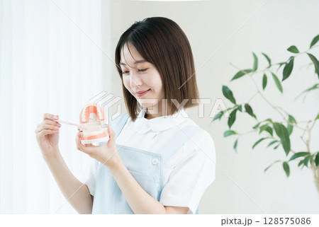 歯ブラシと歯の模型を持つ歯科スタッフの女性 歯ブラシと歯の模型を持つ歯科スタッフの女性 128575086