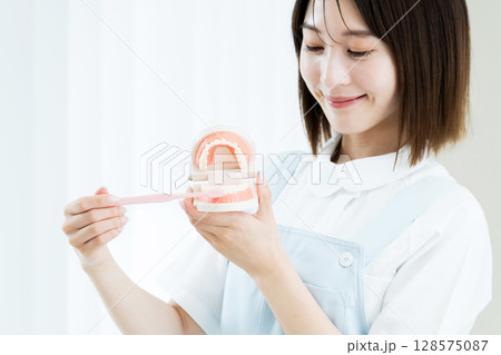 歯ブラシと歯の模型を持つ歯科スタッフの女性 歯ブラシと歯の模型を持つ歯科スタッフの女性 128575087