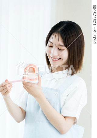 歯ブラシと歯の模型を持つ歯科スタッフの女性 歯ブラシと歯の模型を持つ歯科スタッフの女性 128575089