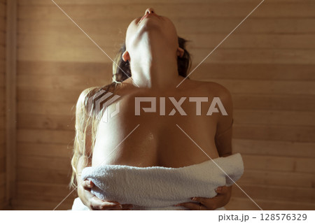 A young woman relaxes and sweats in a hot sauna wrapped in a towel. girl in the sauna. Finnish sauna interior, classic wooden sauna with hot steam. Russian bath. A young woman relaxes and sweats in a hot sauna wrapped in a towel. girl in the sauna. Finnish sauna interior, classic wooden sauna with hot steam. Russian bath. 128576329