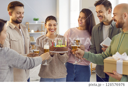 Happy woman holding birthday cake standing at home with friends at evening party. 128576976