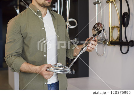 Man holding shower head in plumbing store, close-up Man holding shower head in plumbing store, close-up 128576996