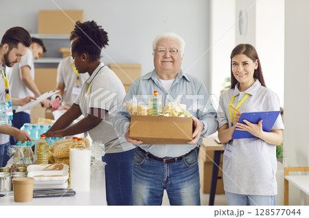 An elderly man at a charity fund holds a box of food, close-up 128577044