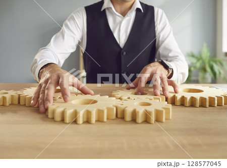 Business man connecting big wooden gears sitting at the desk solving the problem in office. 128577045