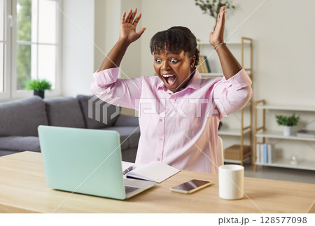 Excited african american woman at home desk in euphoric win online lottery, happy overjoyed Excited african american woman at home desk in euphoric win online lottery, happy overjoyed 128577098