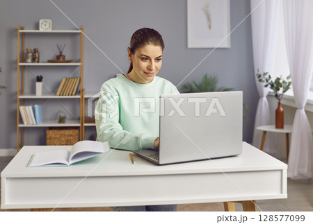 Happy woman sitting at home with laptop on writing desk, close-up 128577099