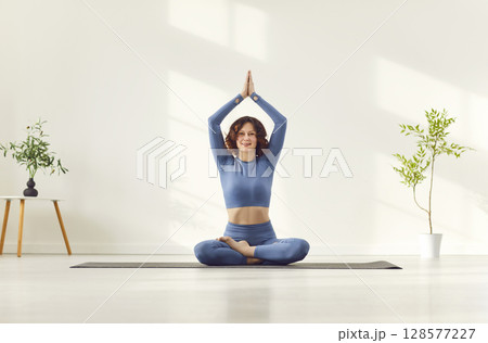 Attractive woman meditating, girl with raised arms up to make Namaste gesture seated in lotus pose Attractive woman meditating, girl with raised arms up to make Namaste gesture seated in lotus pose 128577227