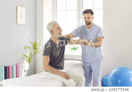 Chiropractor or physical therapist working with senior man's arm in rehabilitation hospital. 128577240