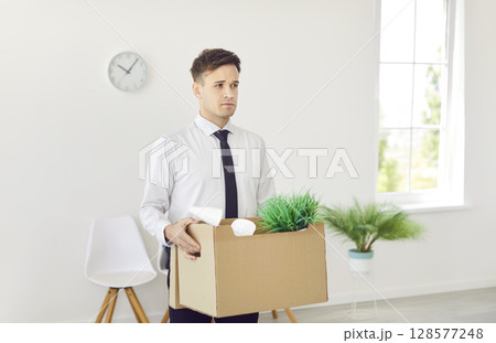 Upset dismissed business man in formal clothes with a box of belongings moving his office. 128577248