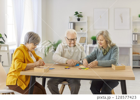 Elderly people sitting at table, solving puzzles, engaging in cognitive activity in nursing home. 128577423