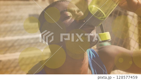 Yellow spots of light against close up of african american fit man drinking water 128577459