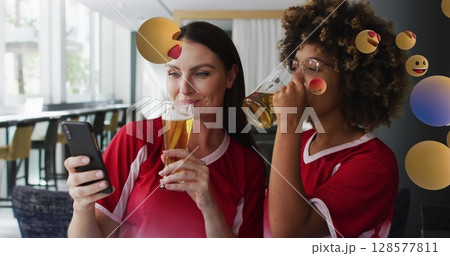 Image of emoji icons over happy diverse female friends using smartphone with beer 128577811