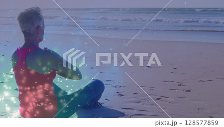 Image of light spots over caucasian woman practicing yoga and meditating at beach Image of light spots over caucasian woman practicing yoga and meditating at beach 128577859