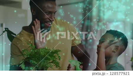 Image of lights over happy african american father and son watering plants and clapping hands 128577921