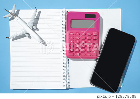 Airplane, notebook, calculator, and cellphone on a blue background. Mockup or Copy space. Travel adventure, navigation, and planning. Concept for travel, tourism, or vacation 128578389