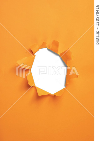 Torn hole in the orange paper reveals a white background. Copy space 128578416