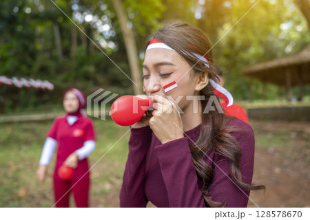 Portrait of an Indonesian southeast asian people celebrate Indonesia Independence Day on the 17th of August with a game of blowing the balloons outdoors. Concept of Kemerdekaan Indonesia 128578670