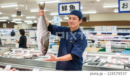 大きな魚を掲げて鮮度をアピールする魚屋の男性店員 128579537