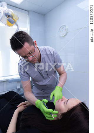 A Professional Dentist Performing Cosmetic Procedure on a Patient Inside a Brightly Lit Dental Clinic with Modern Equipment and Tools for Oral Care and Aesthetics 128579573