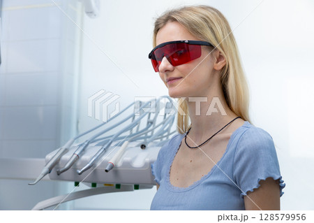 A Woman in a Dental Office Wearing Protective Glasses to Shield Her Eyes from Bright Lights During an Oral Examination or Treatment Session in a Clean Clinic Environment 128579956