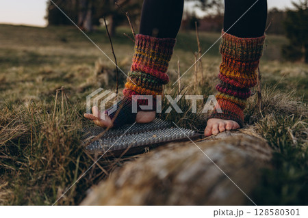 Bare feet in knitted leg warmers standing on nails over grass, symbolizing yoga practice, meditation, pain tolerance, and overcoming fear. A powerful image of mental strength and body awareness Bare feet in knitted leg warmers standing on nails over grass, symbolizing yoga practice, meditation, pain tolerance, and overcoming fear. A powerful image of mental strength and body awareness 128580301