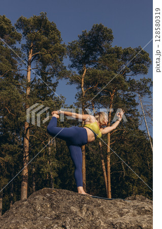 A woman meditating and practicing yoga on top of a rock at sunset, embracing wellness, mindfulness, and eco-friendly living 128580319