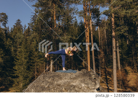 A woman meditating and practicing yoga on top of a rock at sunset, embracing wellness, mindfulness, and eco-friendly living 128580339