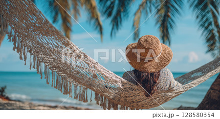 A peaceful scene of relaxation on a tropical beach, featuring a woman enjoying a hammock swing with palm trees, ocean in the background. Perfect for themes of vacation, leisure, and summer tranquility 128580354