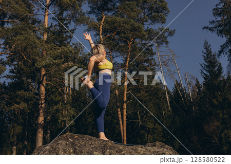 A woman meditating and practicing yoga on top of a rock at sunset, embracing wellness, mindfulness, and eco-friendly living 128580522