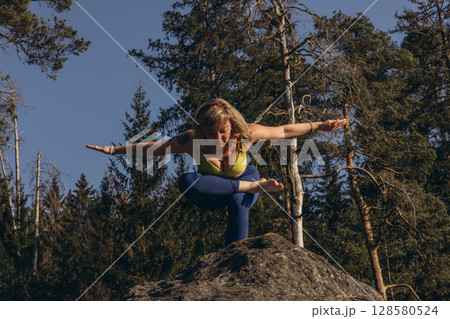 A woman meditating and practicing yoga on top of a rock at sunset, embracing wellness, mindfulness, and eco-friendly living 128580524